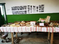 Masă cu față de masă în carouri care prezintă diferite tipuri de pâine și produse de panificație, cu fotografii alb-negru pe peretele din spate.
