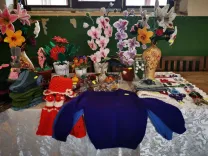 Kézzel készített ruhákat, ékszereket és színes virágdíszeket kínáló piaci stand.