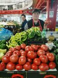 Woman at the market stall with many tomatoes and other vegetables.