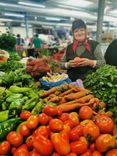 Woman at vegetable stand with tomatoes, carrots and other vegetables.