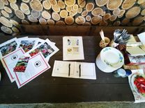 Asztal brosúrákkal, könyvekkel, tányérokkal és néhány paradicsommal a fakupacok háttere előtt.