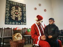 O persoană în costum de Moș Crăciun stă și vorbește cu un copil într-o cameră.