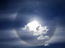 Sonne hinter Wolken mit einem leichten Regenbogen-Halo.