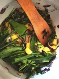 Bowl of various vegetables and herbs mixed with pieces of yellow ingredients, stirred with a wooden spoon.