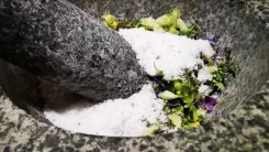 A mortar with crushed herbs and white powder, probably salt, mixed and crushed with a stone pestle.