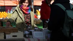 Andrea at her market stall selling products while customers look on.