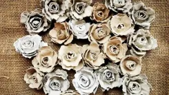 Ansammlung von handgemachten Blumen aus Papier oder dünnem Stoff auf einem groben, sackartigen Untergrund.